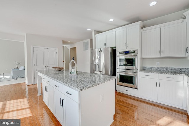 kitchen with white cabinets, appliances with stainless steel finishes, light stone counters, and light wood finished floors