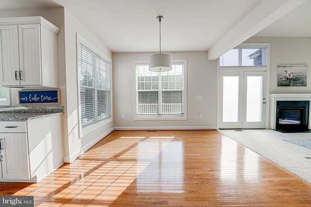 unfurnished dining area featuring baseboards, light wood finished floors, and a glass covered fireplace
