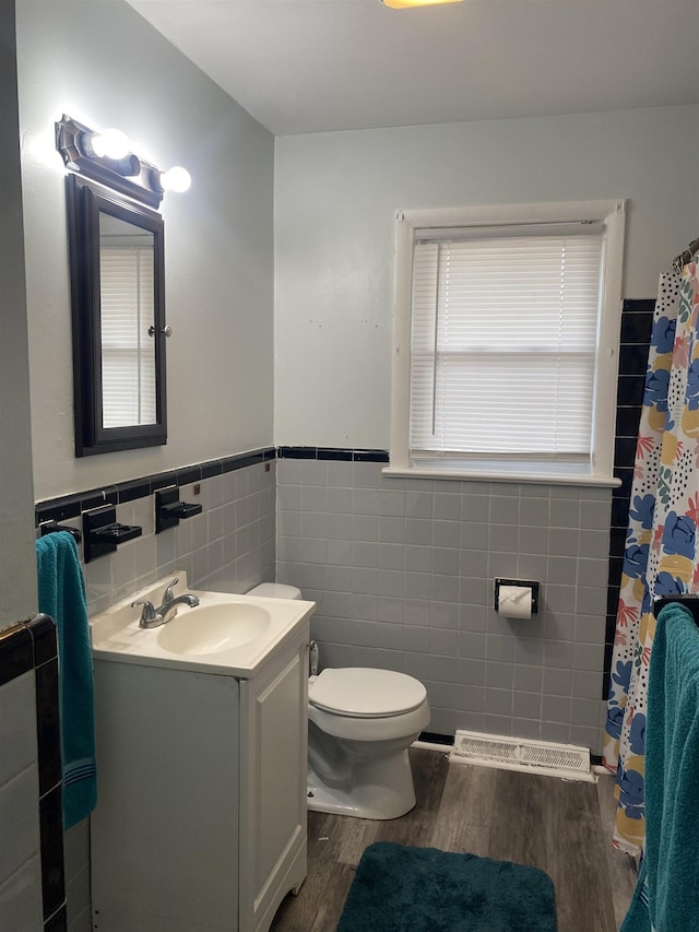 bathroom with toilet, wood finished floors, vanity, tile walls, and wainscoting