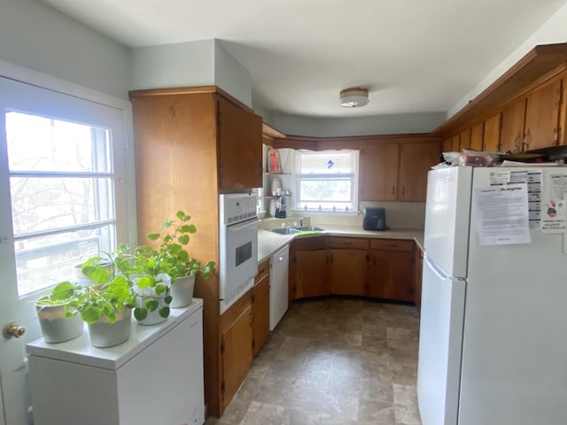 kitchen featuring light countertops, white appliances, a sink, and brown cabinets