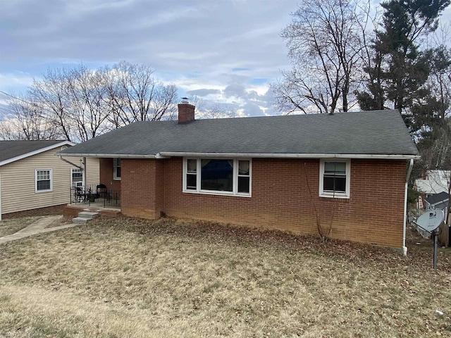 rear view of property featuring roof with shingles, brick siding, and a chimney