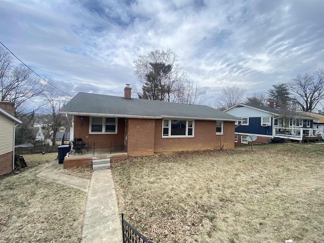 view of front of house with brick siding, roof with shingles, a chimney, a front yard, and fence