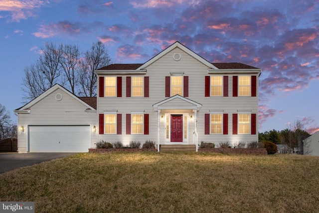 colonial-style house featuring aphalt driveway, a lawn, and an attached garage