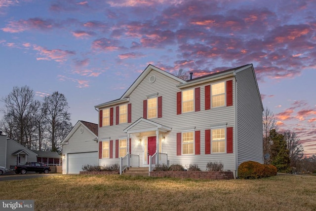 colonial-style house featuring an attached garage, driveway, and a front lawn