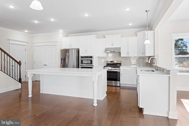 kitchen featuring a kitchen island, under cabinet range hood, a kitchen bar, stainless steel appliances, and a sink