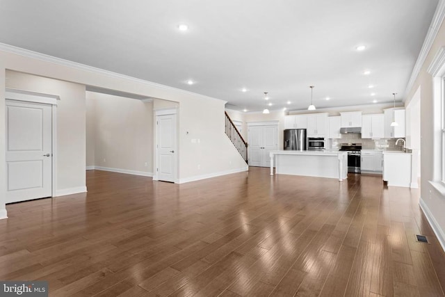 unfurnished living room featuring stairway, baseboards, dark wood-style flooring, a sink, and ornamental molding