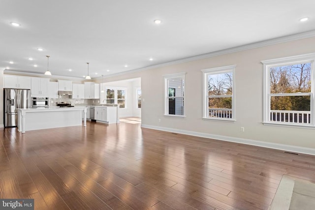 unfurnished living room with a wealth of natural light, dark wood-style flooring, and crown molding