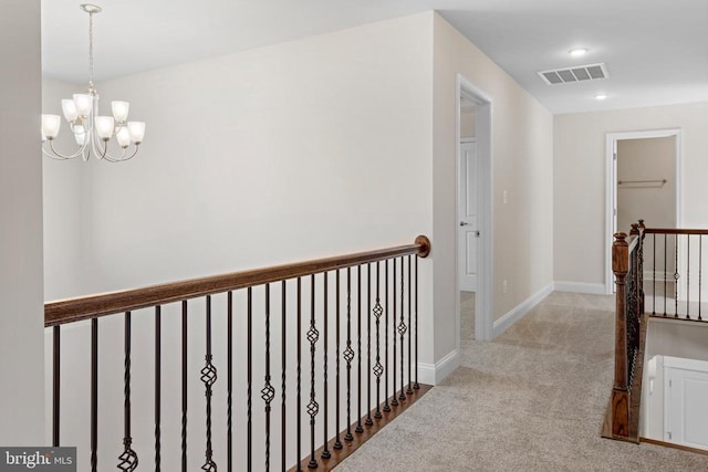 hall with visible vents, an upstairs landing, an inviting chandelier, carpet flooring, and baseboards