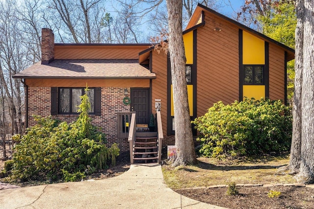 view of front facade featuring a shingled roof, brick siding, and a chimney