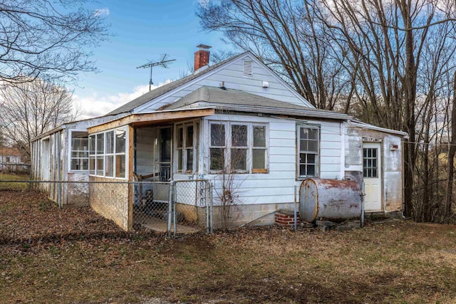 view of front of home featuring heating fuel, fence, a sunroom, and a chimney