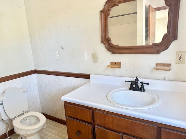 half bath featuring toilet, wainscoting, vanity, and tile patterned floors