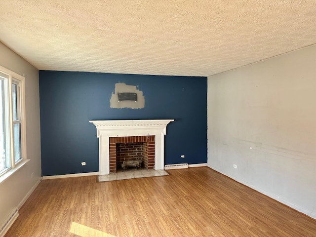 unfurnished living room featuring a brick fireplace, a baseboard heating unit, a textured ceiling, and light hardwood / wood-style floors