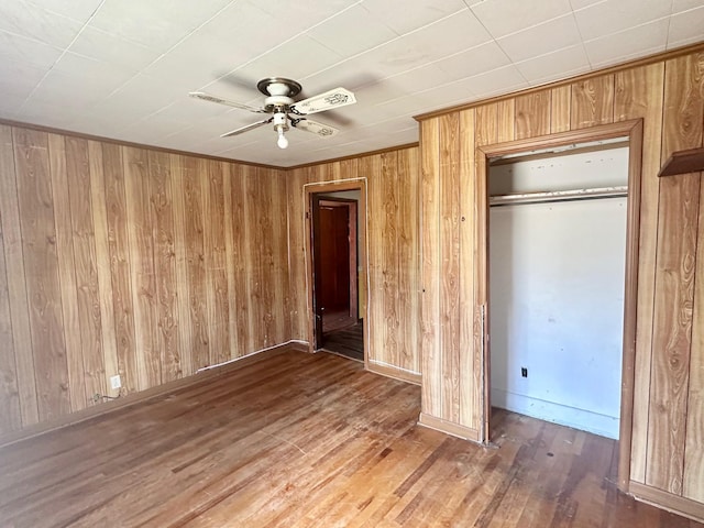 unfurnished bedroom featuring wooden walls, baseboards, a ceiling fan, wood finished floors, and a closet