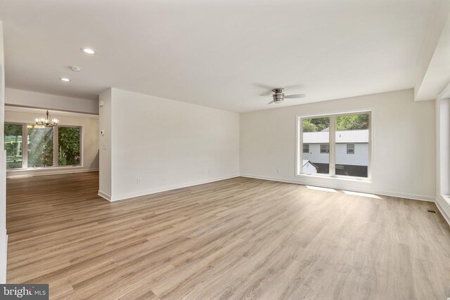 empty room featuring ceiling fan with notable chandelier and light hardwood / wood-style floors