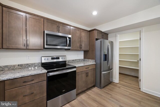 kitchen with dark brown cabinetry, light wood-type flooring, light stone countertops, and appliances with stainless steel finishes