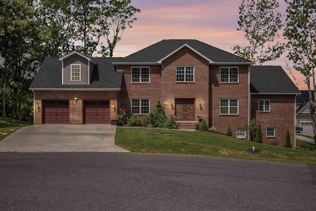 colonial-style house featuring a garage, a shingled roof, concrete driveway, a yard, and brick siding