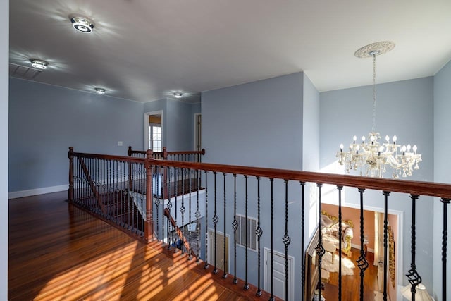 hallway featuring baseboards, dark wood-type flooring, an upstairs landing, and a notable chandelier