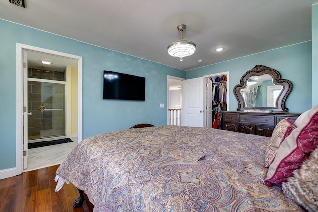 bedroom featuring baseboards, ensuite bath, wood finished floors, a spacious closet, and a closet