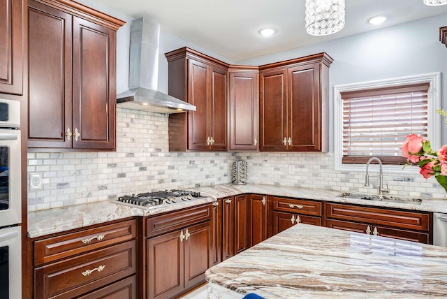 kitchen with light stone counters, stainless steel appliances, a sink, decorative backsplash, and wall chimney exhaust hood