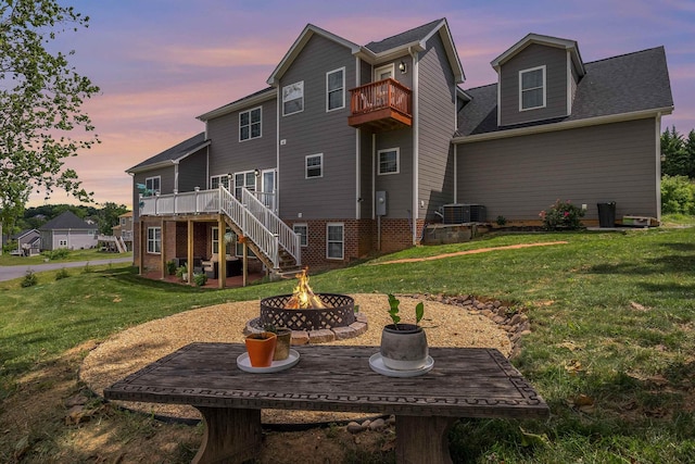 back of property with stairs, a fire pit, a lawn, and a wooden deck