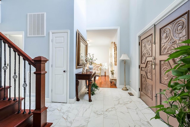 foyer featuring marble finish floor, baseboards, stairway, and visible vents