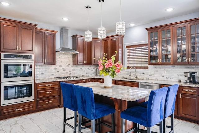 kitchen featuring stainless steel appliances, a sink, a center island, wall chimney exhaust hood, and glass insert cabinets