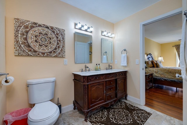 full bathroom with double vanity, toilet, ensuite bathroom, a sink, and baseboards