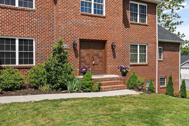 entrance to property featuring roof with shingles, a lawn, and brick siding