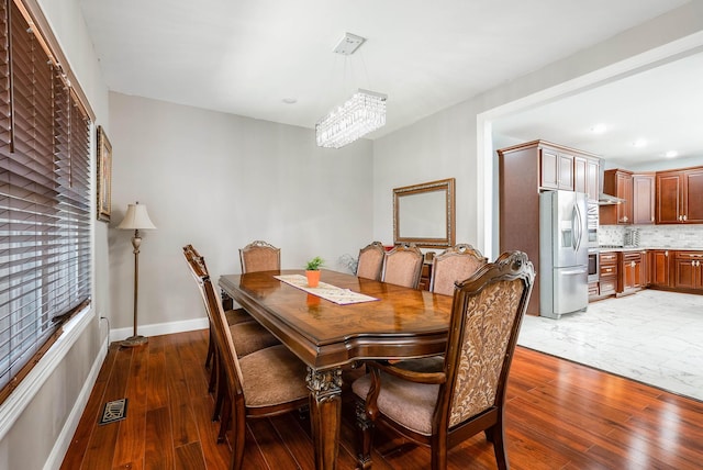 dining space featuring baseboards, hardwood / wood-style floors, visible vents, and a notable chandelier