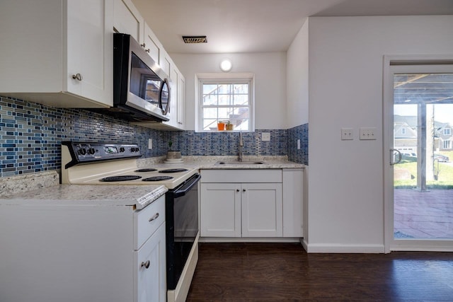 kitchen with electric range oven, stainless steel microwave, light stone counters, white cabinetry, and a sink