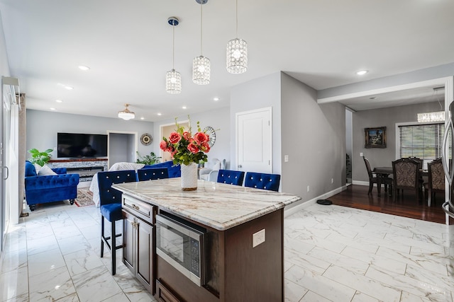 kitchen featuring marble finish floor, stainless steel microwave, a kitchen island, and a kitchen breakfast bar