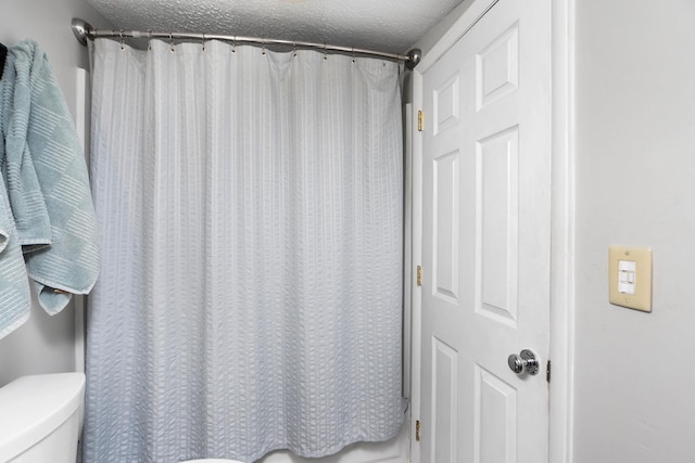 full bath featuring toilet, curtained shower, and a textured ceiling