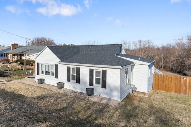 view of property exterior with a shingled roof, fence, and a lawn