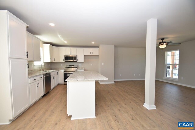 kitchen featuring sink, stainless steel appliances, a center island, light stone counters, and white cabinets