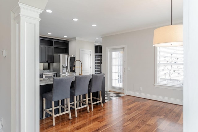 kitchen with a kitchen bar, dark hardwood / wood-style flooring, stainless steel fridge, light stone countertops, and decorative columns