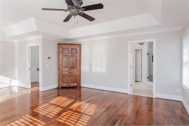 empty room featuring wood-type flooring, ceiling fan, crown molding, and a tray ceiling