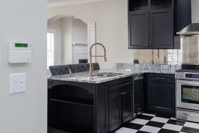 kitchen featuring sink, stainless steel stove, light stone counters, kitchen peninsula, and wall chimney exhaust hood