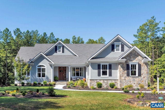 craftsman house featuring stone siding, a shingled roof, and a front yard