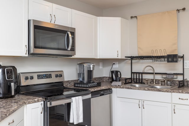 kitchen featuring dark countertops, appliances with stainless steel finishes, white cabinetry, and a sink