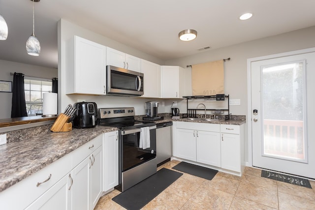 kitchen with visible vents, a sink, appliances with stainless steel finishes, white cabinetry, and decorative light fixtures