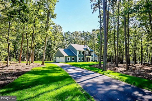 view of front of property with driveway, a wooded view, and a front yard