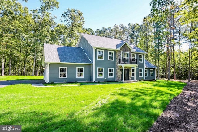 colonial home featuring stone siding, a front lawn, and roof with shingles