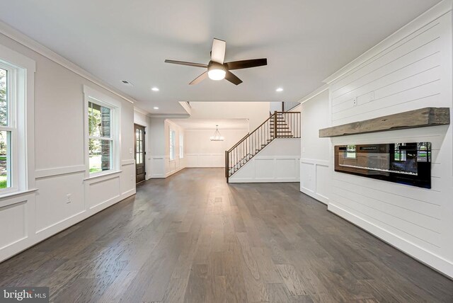 unfurnished living room with ornamental molding, dark wood-type flooring, and ceiling fan with notable chandelier