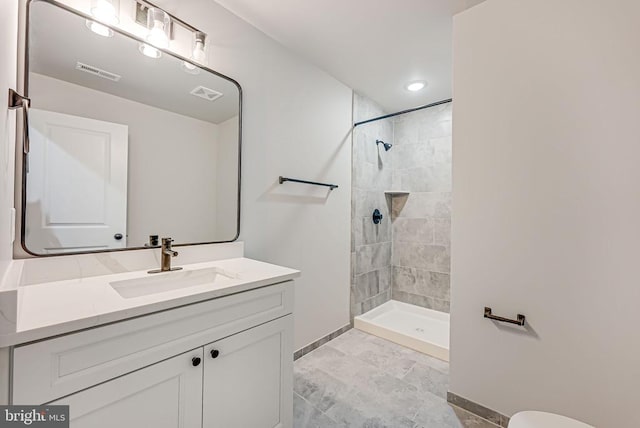 bathroom with baseboards, visible vents, tiled shower, and vanity