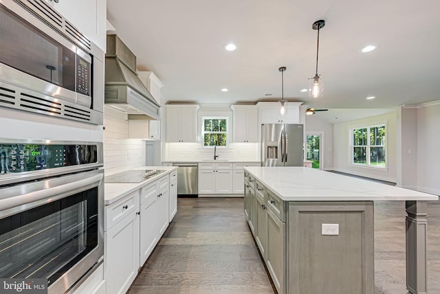 kitchen with a kitchen island, white cabinetry, hanging light fixtures, stainless steel appliances, and light stone countertops