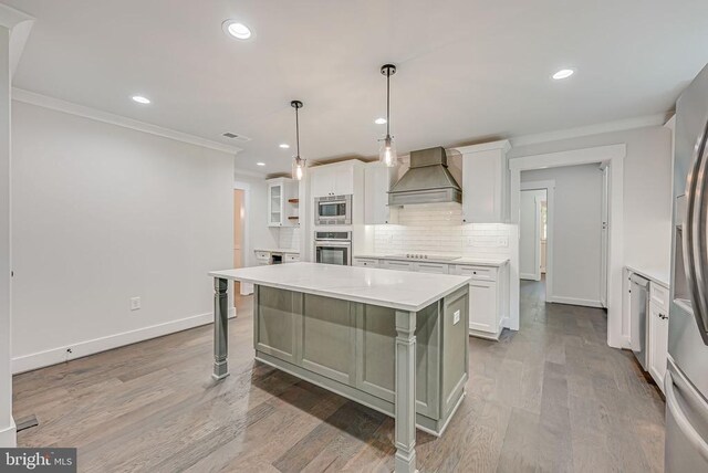 kitchen featuring a kitchen island, white cabinets, hanging light fixtures, stainless steel appliances, and custom range hood