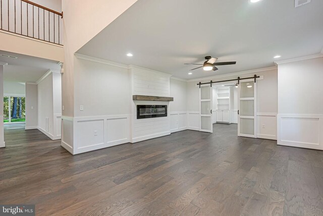 unfurnished living room with a ceiling fan, crown molding, dark wood finished floors, and a barn door