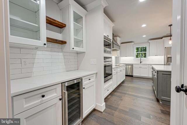 kitchen with appliances with stainless steel finishes, pendant lighting, white cabinetry, beverage cooler, and dark hardwood / wood-style flooring