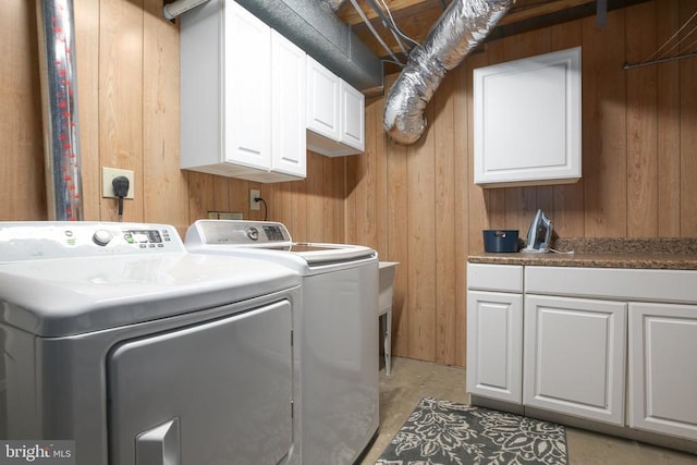 clothes washing area with cabinet space, wooden walls, and independent washer and dryer