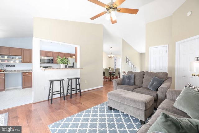 living area featuring baseboards, ceiling fan with notable chandelier, high vaulted ceiling, and light wood-style floors